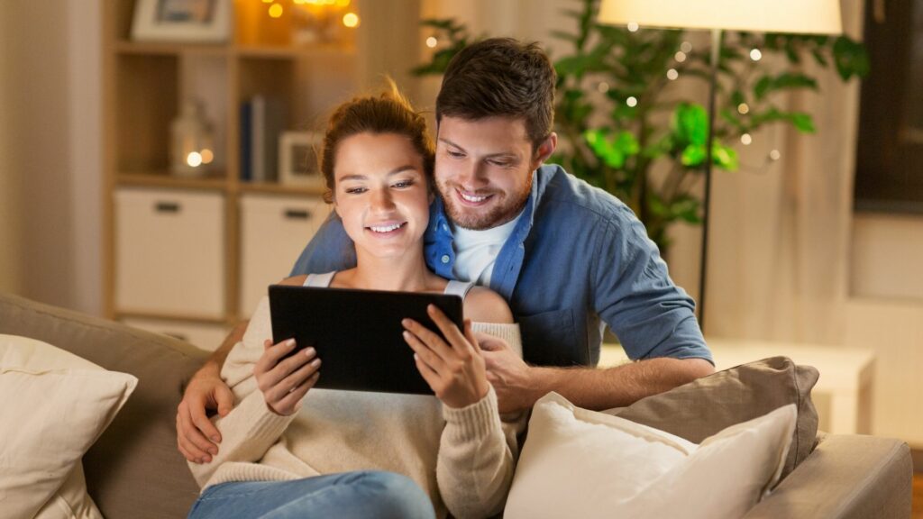 Coppia felice utilizza un tablet comodamente da casa per accedere ai servizi fiscali di un CAF online, risolvendo le pratiche in modo semplice e veloce.